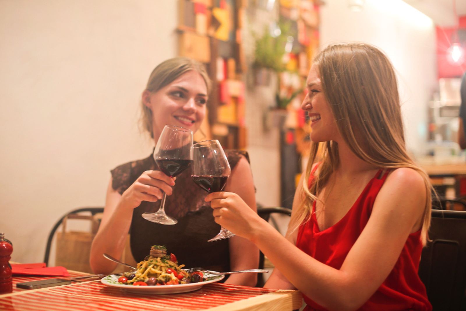 Two friends laughing and raising glasses at a restaurant table, with no phones in sight
