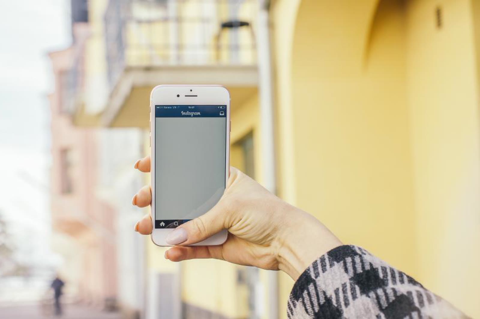A hand holding up a phone with Instagram open, buildings in the background