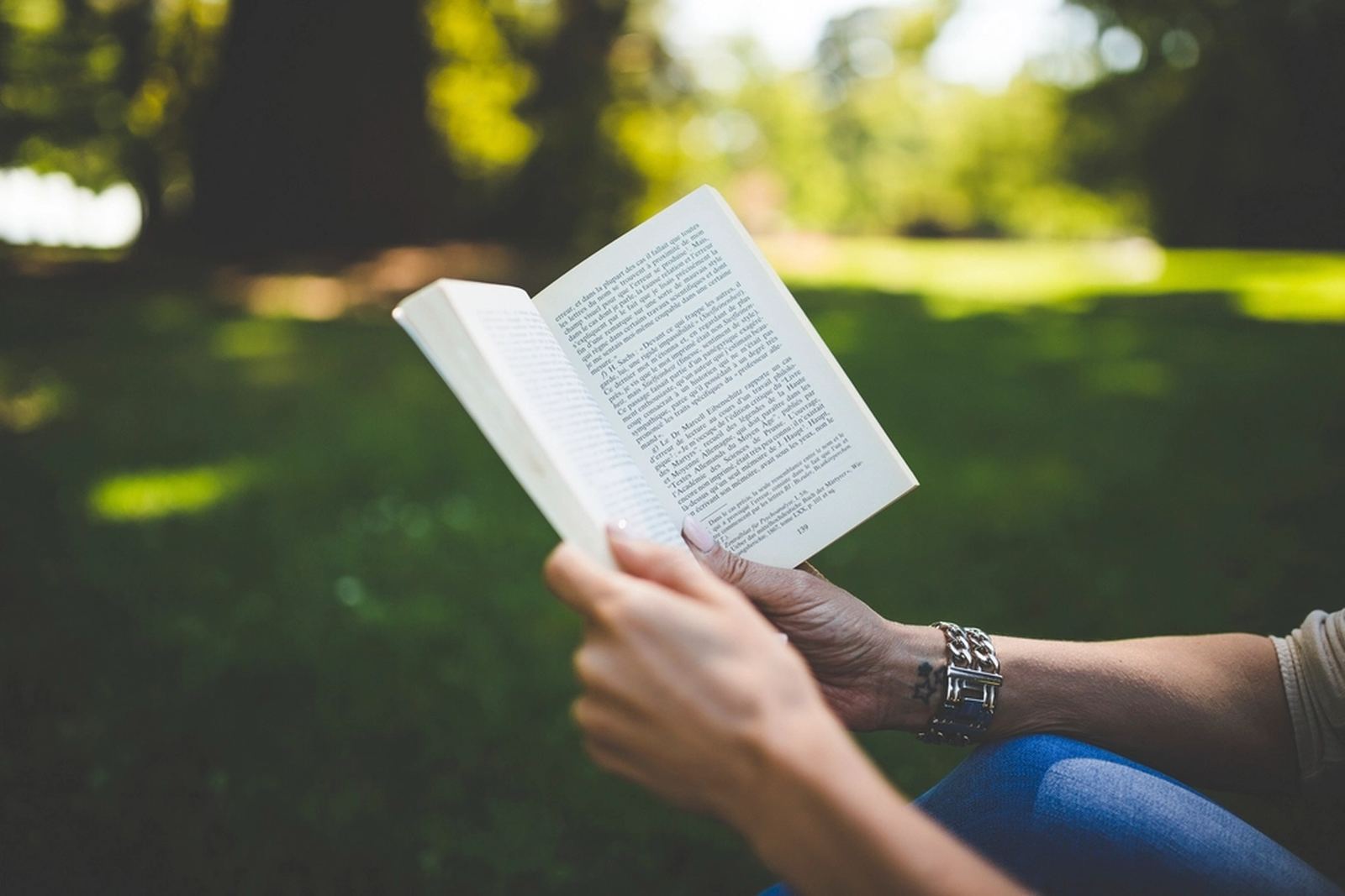 Hands holding an open book outdoors in the sun