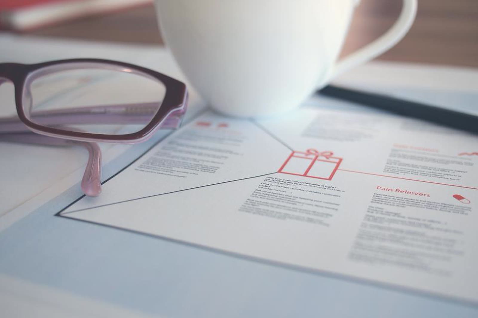 Reading glasses and a coffee cup on a desk covered in notes