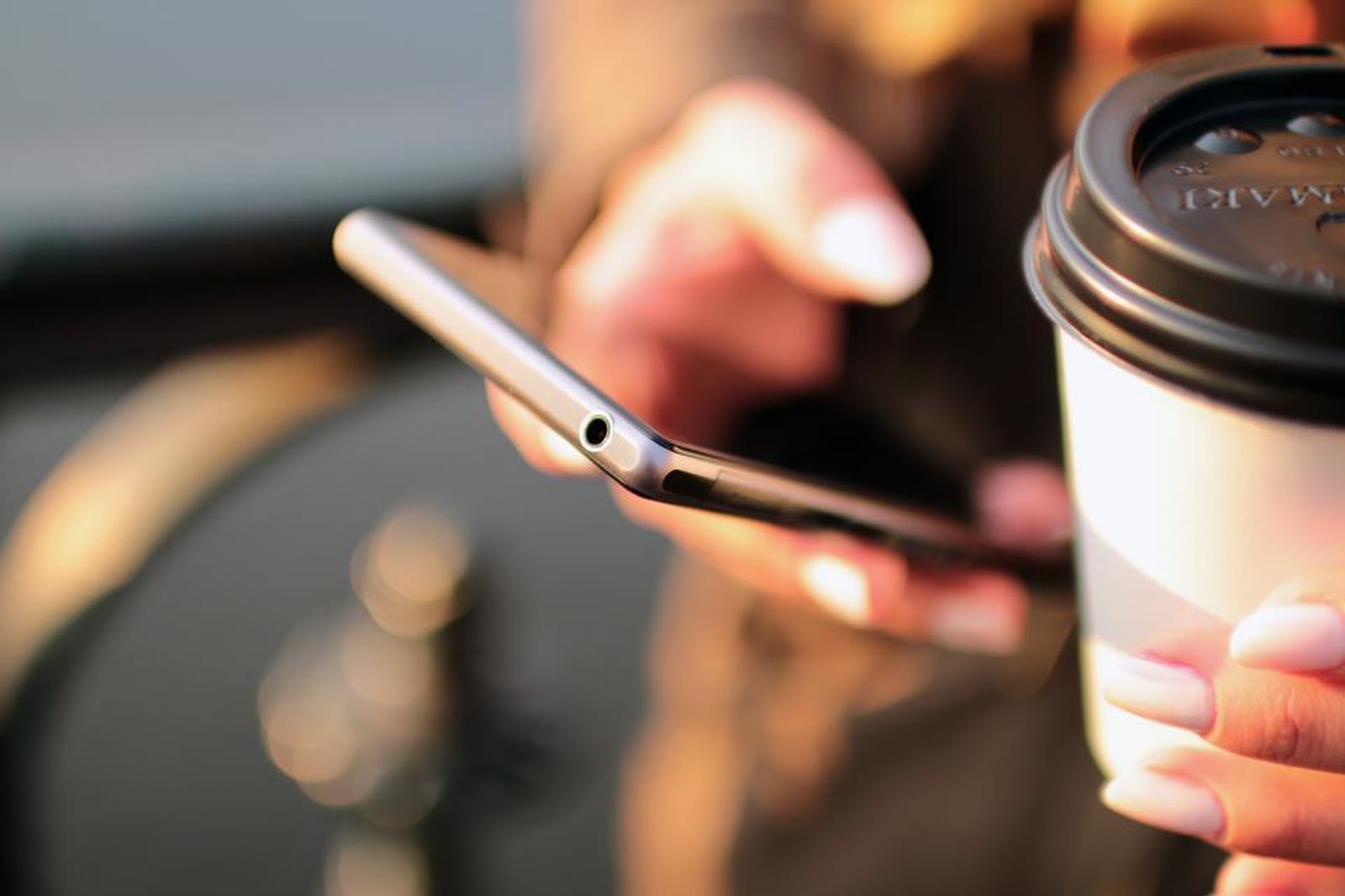 A hand holding a phone next to a takeaway coffee cup